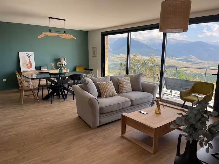 Salon lumineux avec canapé, coin repas et vue dégagée sur la montagne